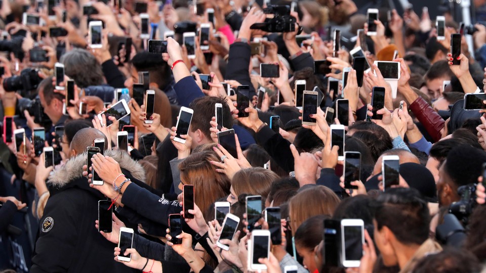 A crowd of people hold up their phones.