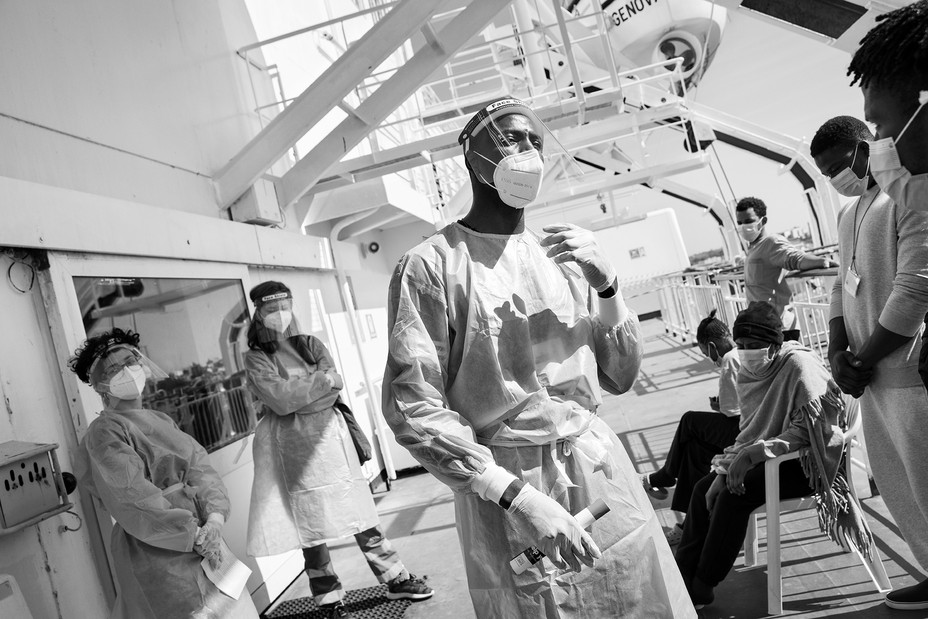 Red Cross workers and migrants on the deck of the ship wearing face masks