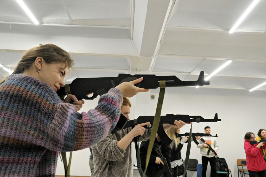 Several civilians practice handling weapons, using wooden replicas at a training session.