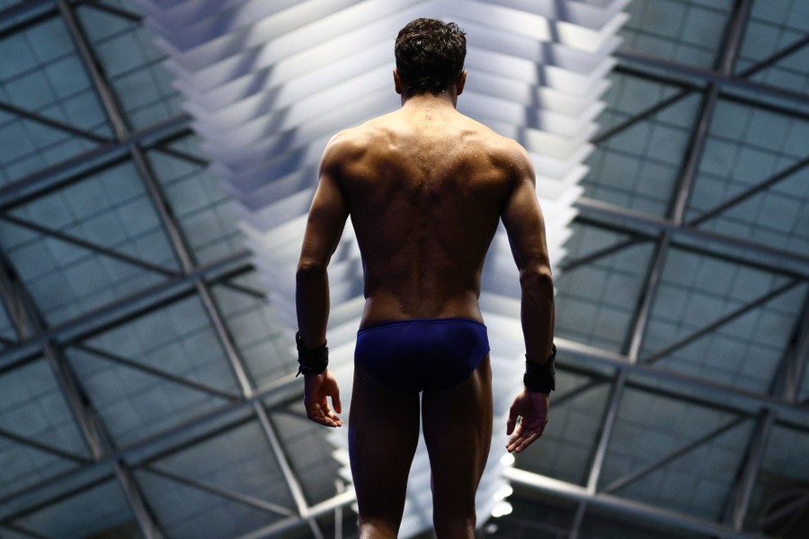 A diver wearing a swimsuit stands ready to jump, seen from behind.