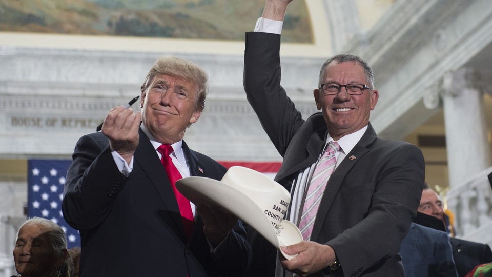 President Trump holds up a pen while another man holds up a cowboy hat.