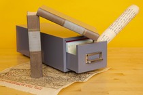 A filing cabinet drawer on a wooden floor, against a yellow background, with history books and a map