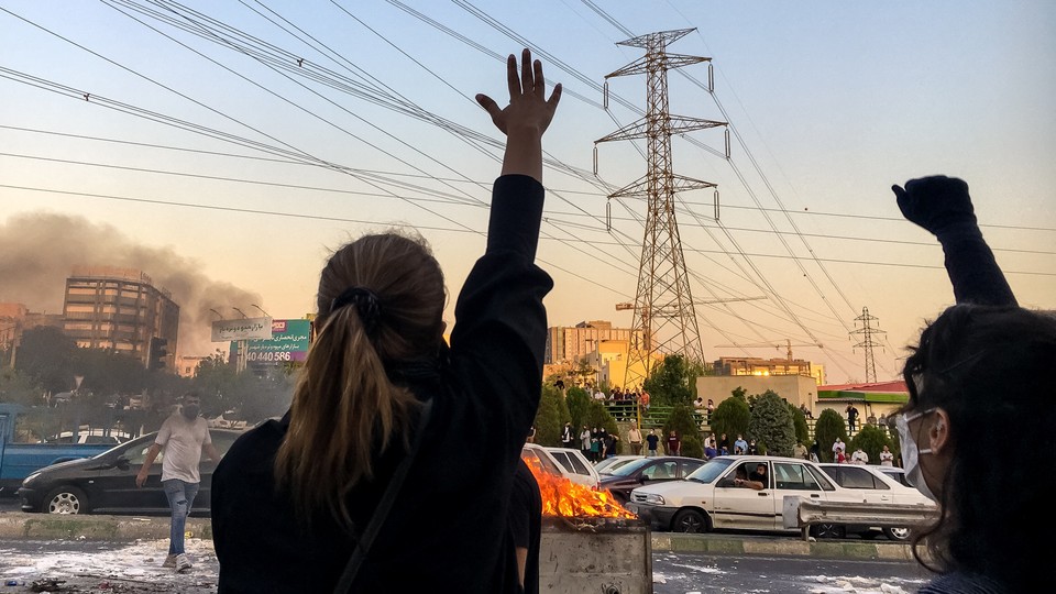 Women raise their hands in protest in front of a burning dumpster during the 2022 demonstrations in Tehran