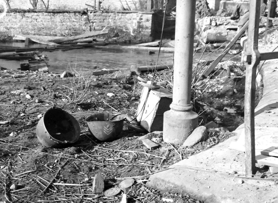 A U.S. soldier's helmet and helmet liner lie on the ground, among other scattered debris.