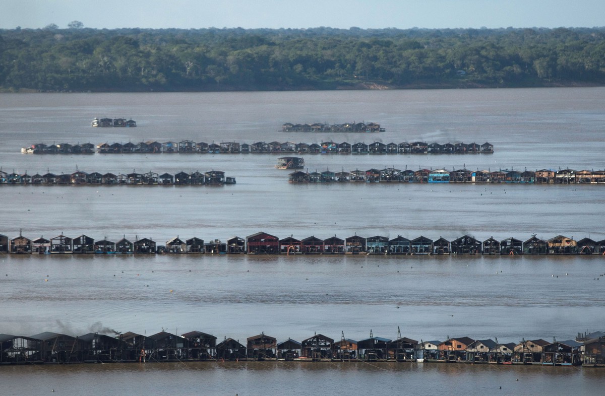An aerial view shows dozens of dredging rafts lashed together in several lines, floating on a large river.