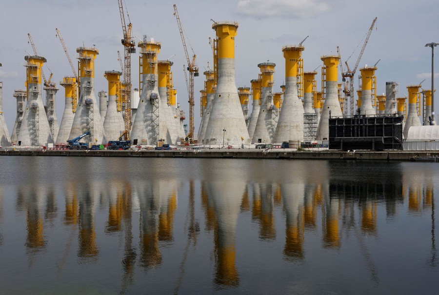 Rows of wind-turbine support platforms surrounded by cranes and reflected in a body of water below