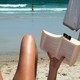 someone reads a book on the beach, their legs are visible