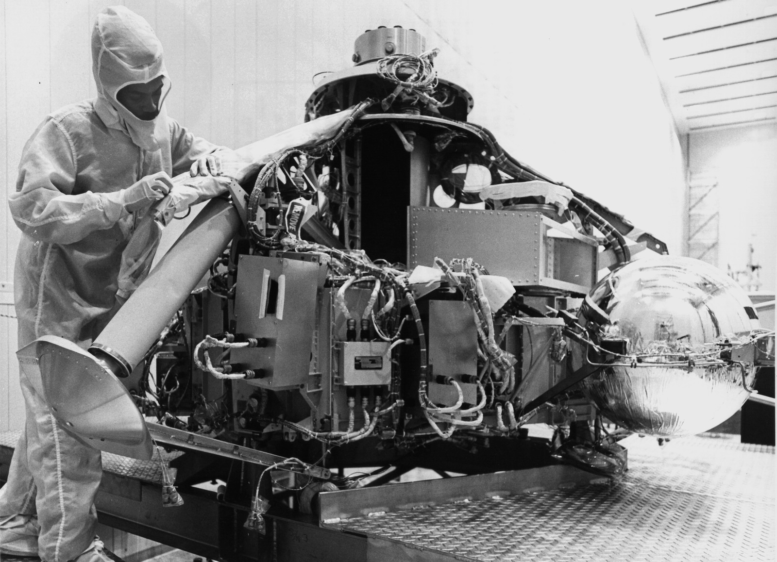 A person wearing a protective suit works on the interior of a spacecraft as it's being assembled.
