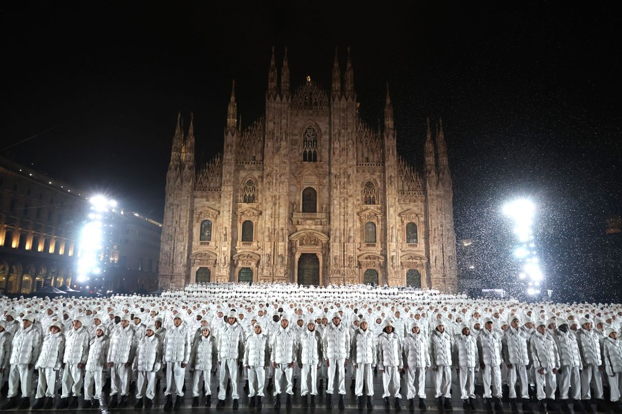 Hundreds of models wearing white winter gear stand together in front of a cathedral.