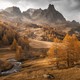 A broad view of an alpine valley and stony mountains with trees and grass a golden color.