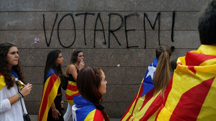 Students wear Esteladas (Catalan separatist flag) during a demonstration in front of a graffiti on the wall that reads, "We will vote!"