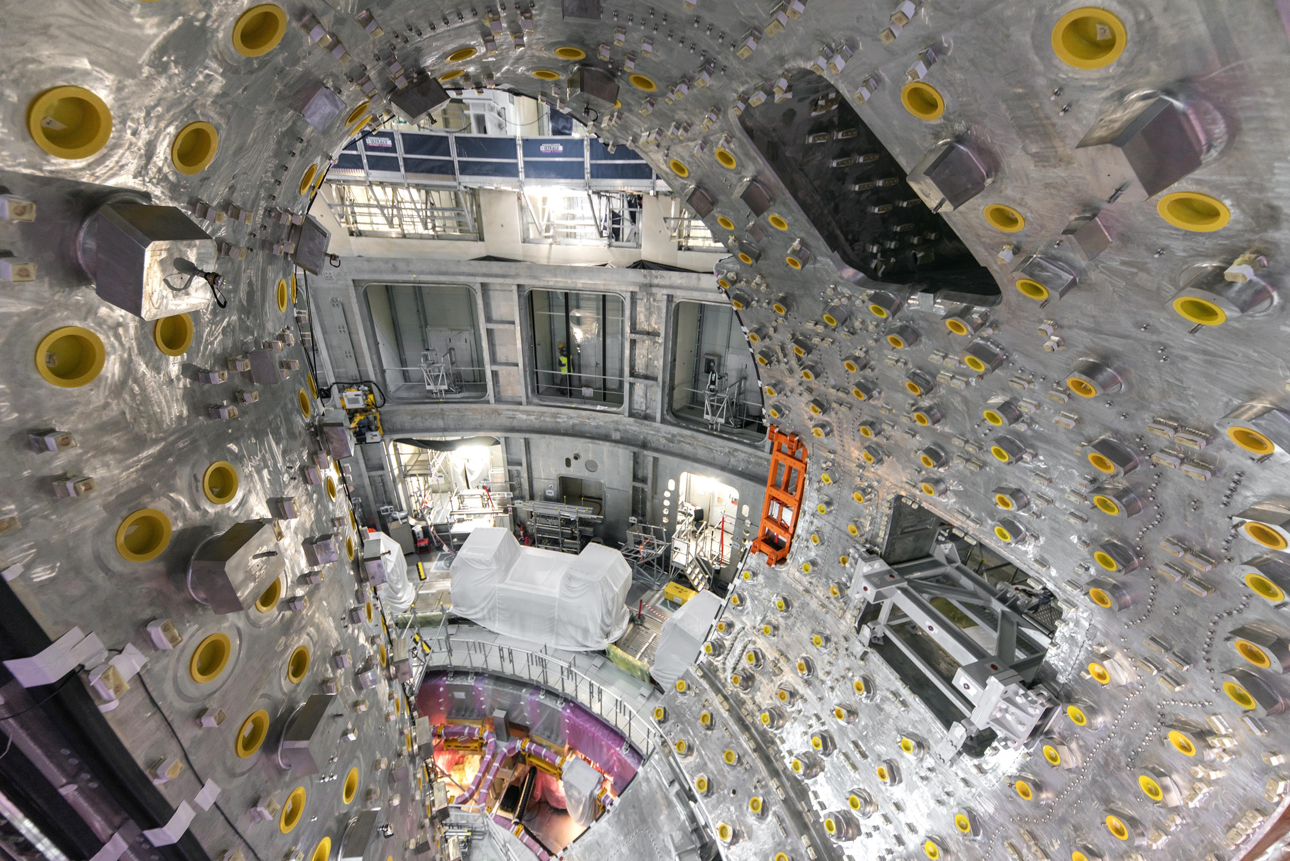 The interior of a partially completed torus-shaped fusion chamber, studded with small and large attachment points