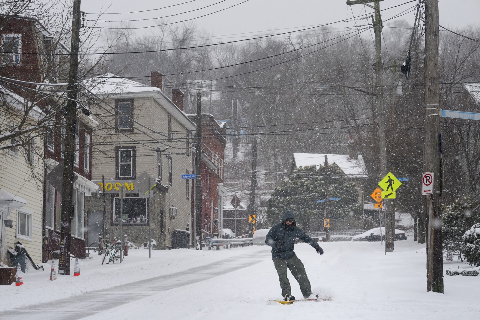 A person snowboards down a snowy street.