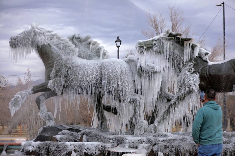 A man takes a picture of an ice-covered statue of horses.