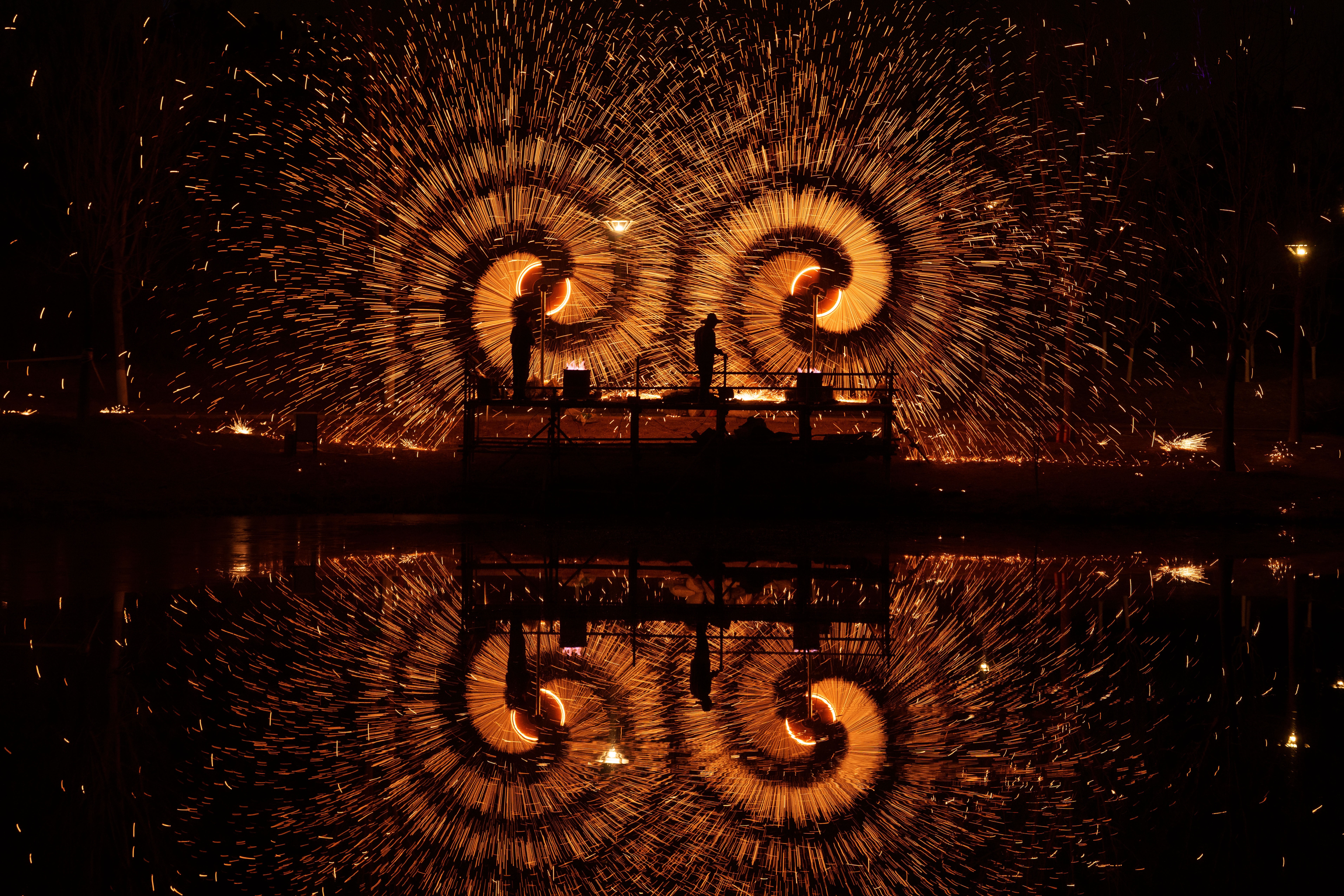 People on a stage send bits of molten iron flying from spinning mechanisms, making bright spiral shapes in the air.
