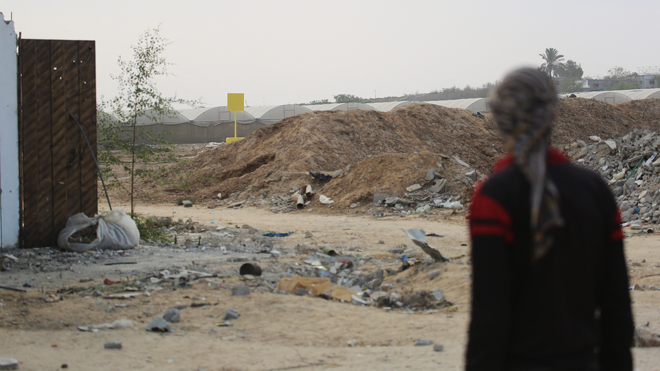 A Palestinian man in the foreground faces the direction of a concrete block marking the "yellow line" in the background.