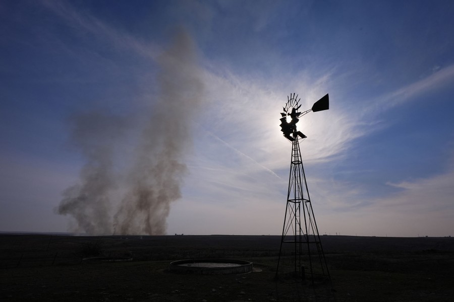 Smoke billows above a field near a windmill during a wildfire.