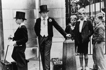 A black-and-white photo depicting local boys staring at Harrow schoolboys in coats and top hats.