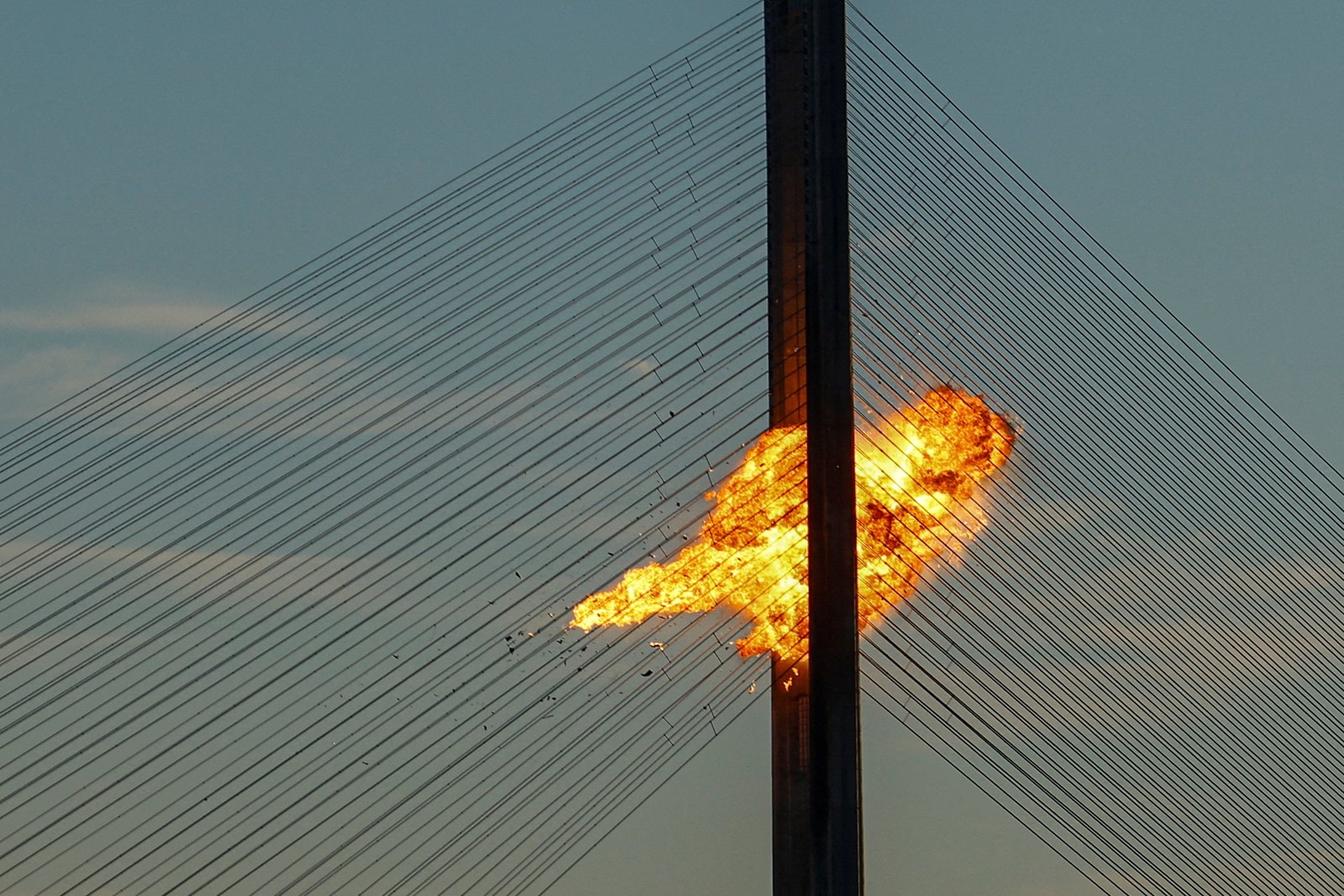 A drone explodes in a fireball between two tall bridge supports.