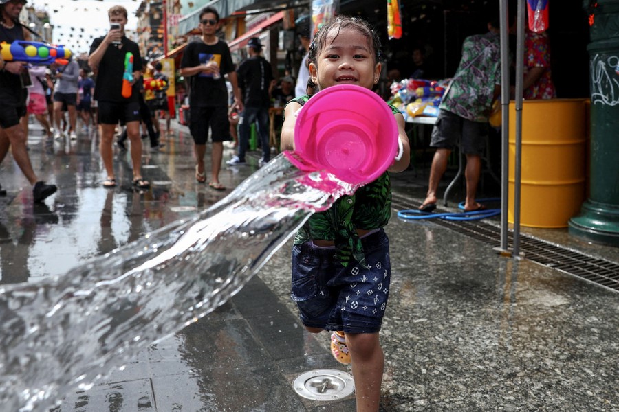 A girl playfully throws a bucket of water in a street.