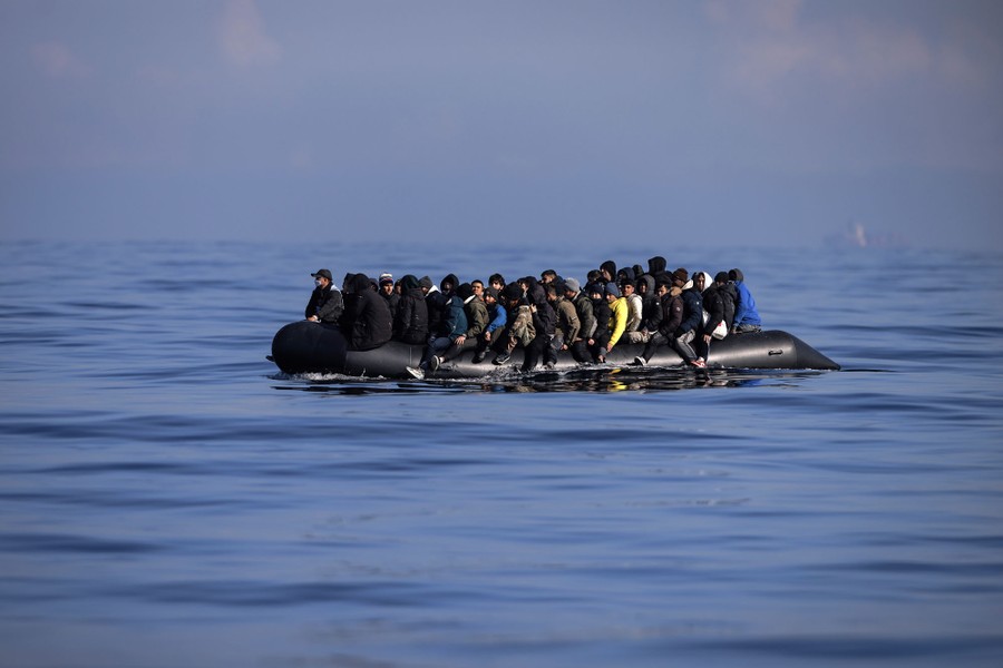An overloaded inflatable dinghy carries dozens of people in open ocean water.