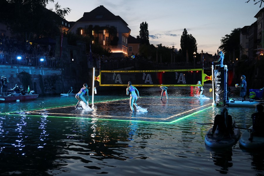 Two 2-person teams play a game of volleyball on a partially-submerged court located on the surface of a river.