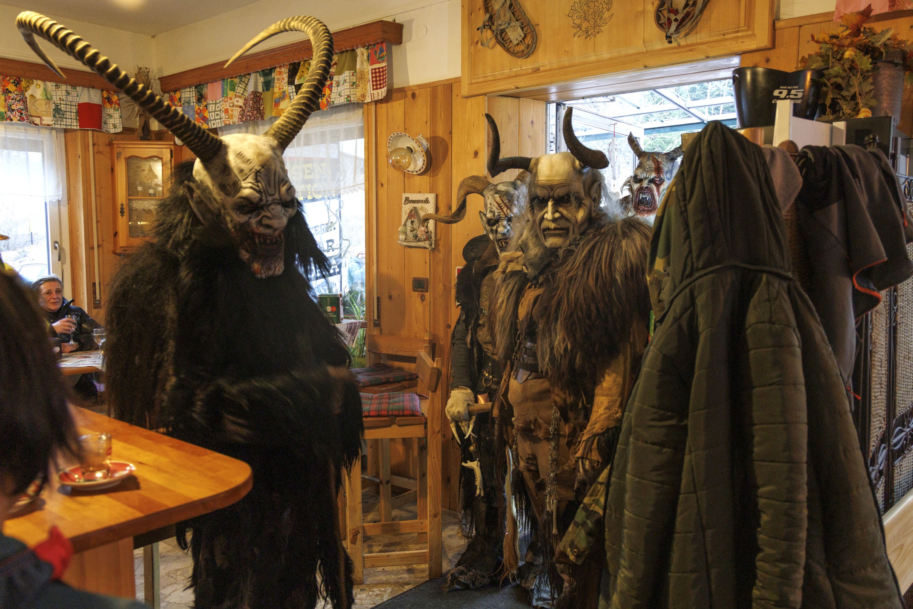 Several performers dressed as Krampus walk into a well-lit bar.