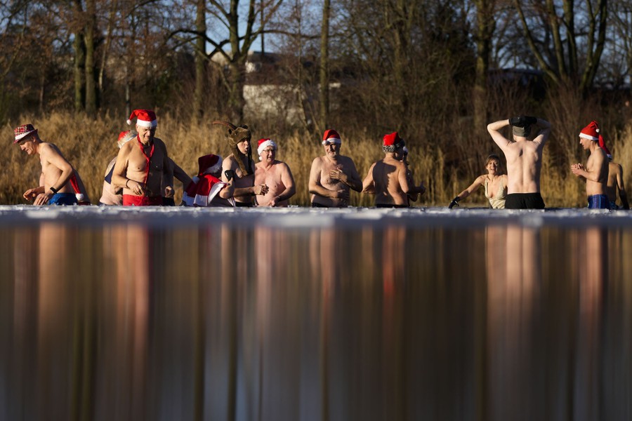 About a dozen people are seen, wearing Santa hats and swimsuits, in waist-deep water.