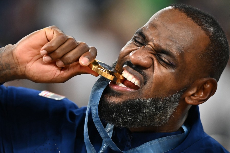 Basketball player LeBron James playfully bites a gold medal.