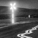 A black-and-white photo of a glowing white traffic sign and a swirly white line on the ground, with a hill in the background