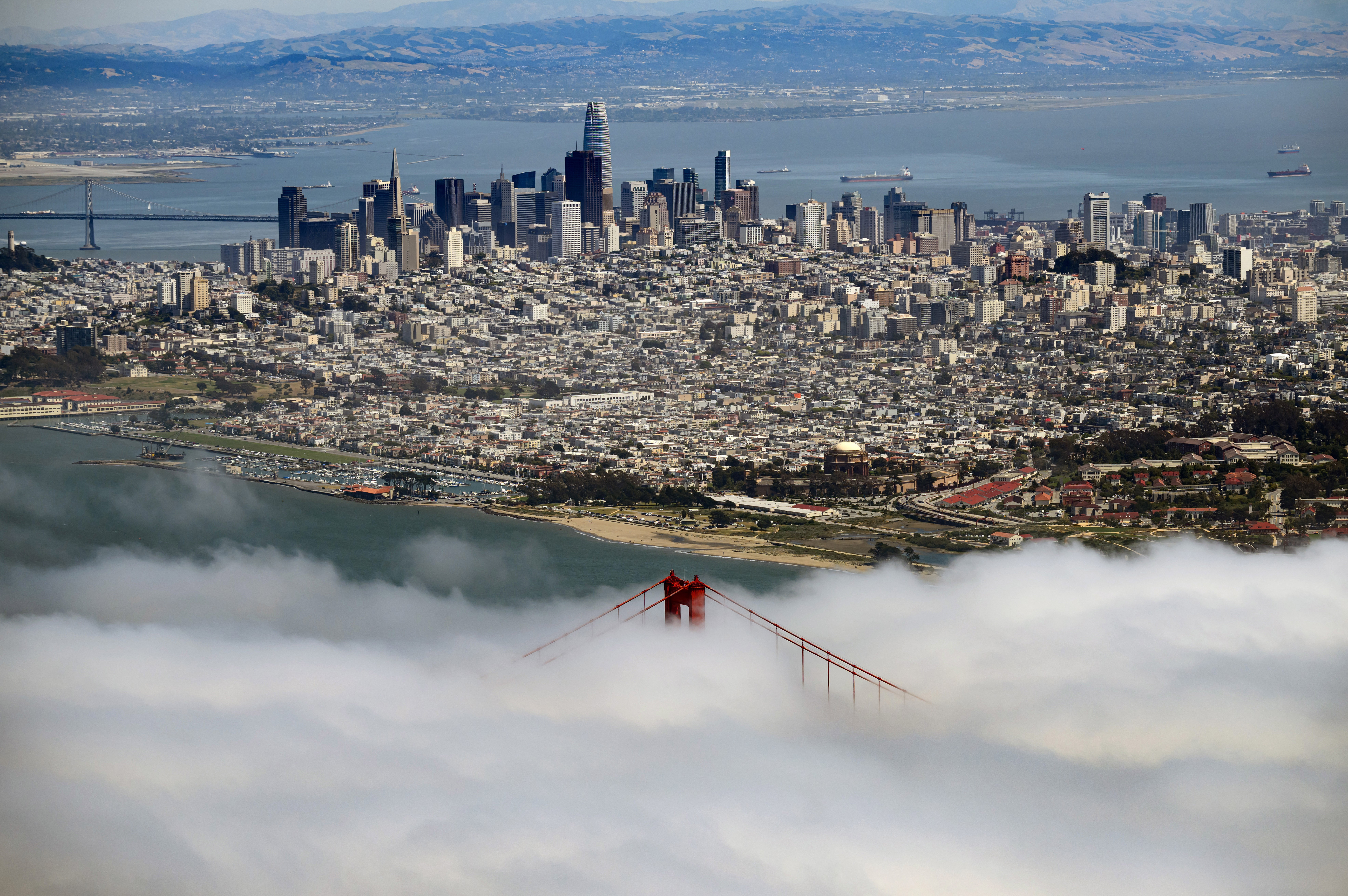 Fog rolls by the Golden Gate Bridge in San Francisco, with the city seen beyond, untouched by the fog.