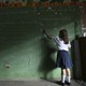 A child writes on a large chalkboard. Half the image is in shadows.