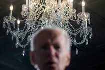 A photo of Joe Biden, blurred in foreground, in front of a chandelier in focus behind.