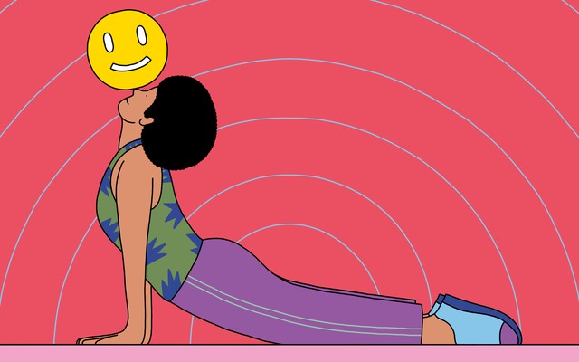 A woman in the upward-dog yoga pose balancing a smiley face on her nose