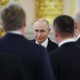 Several men in suits stand with their backs to the camera while Putin faces it head-on, in sharp focus