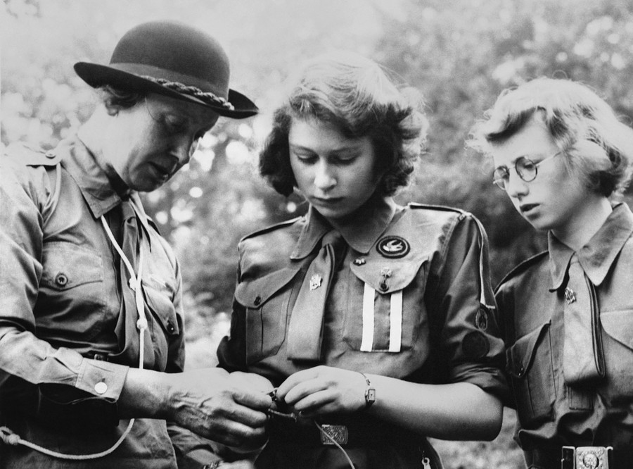 A woman in uniform shows two younger women how to tie a knot.