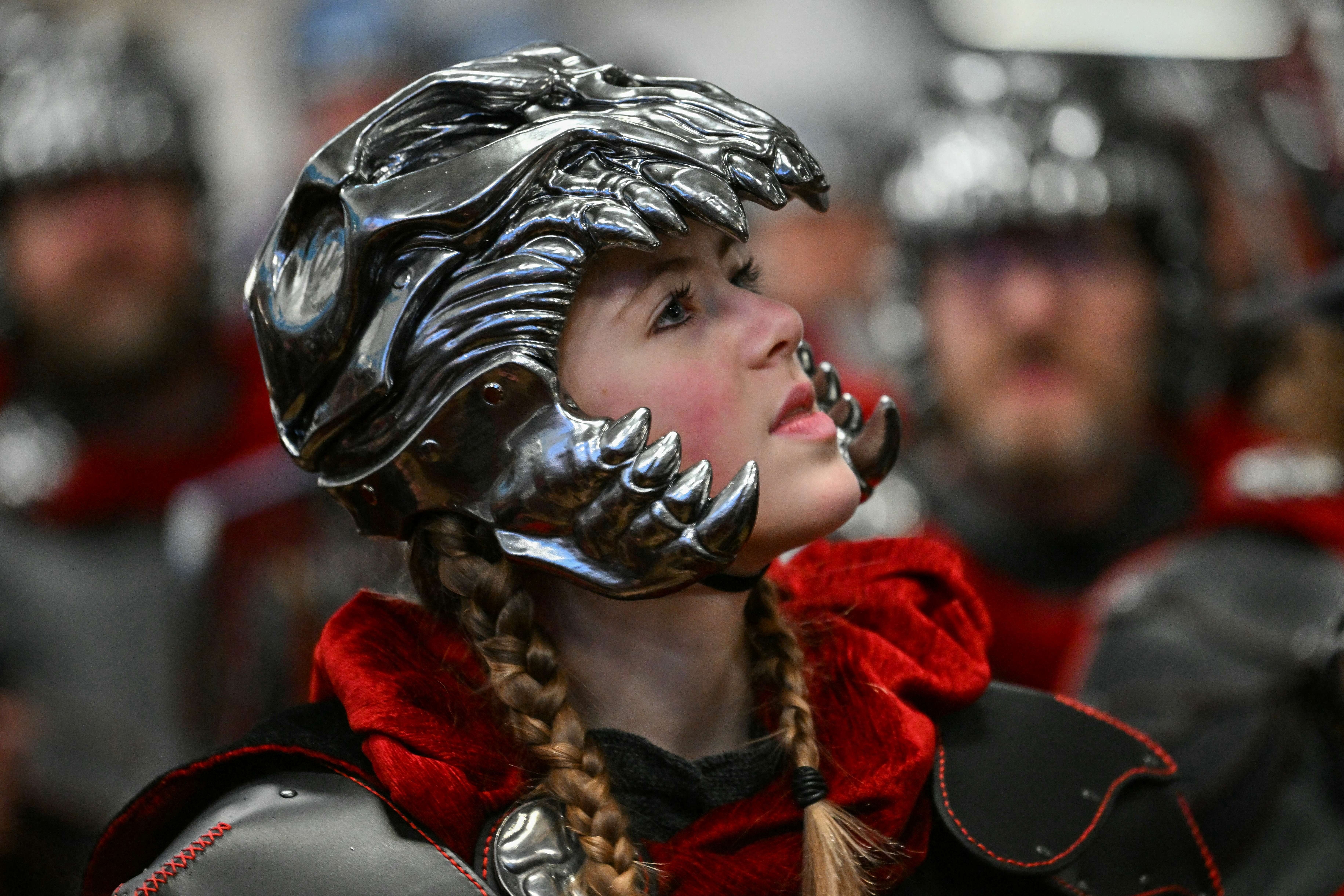 A person wears a metallic-looking helmet shaped like the skull of a fearsome monster.