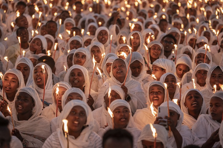 A large group of people hold candles while singing.