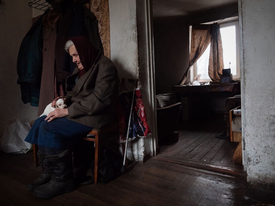 An older woman sits in a chair in a room, holding a small dog.