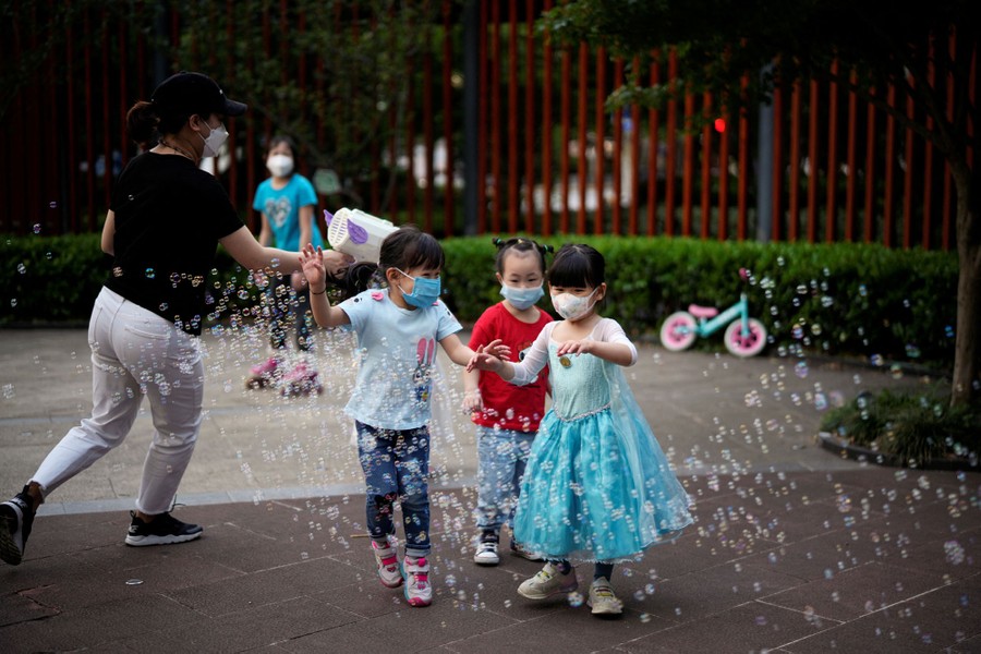 Three children play in a park, amid a small cloud of bubbles.