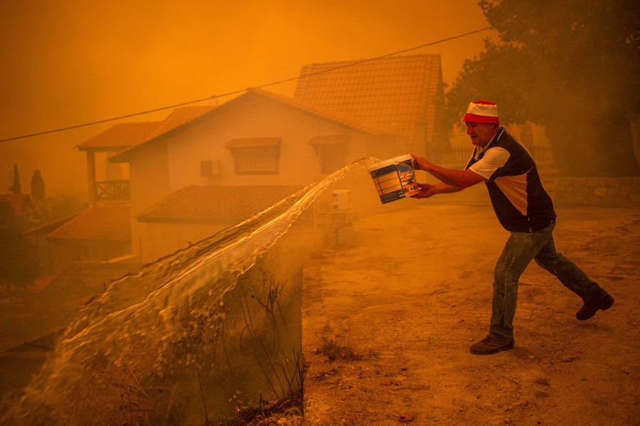 A person throws a bucket of water in a village under a smoky sky.
