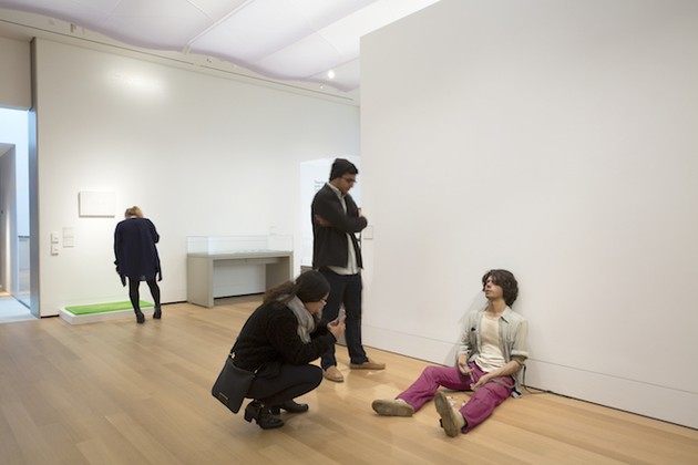Two patrons observe the sculpture of a man sitting dejectedly on the floor.