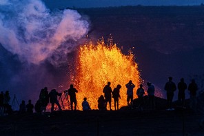 A crowd of onlookers pictured in silhouette against a fountain of erupting lava in the distance