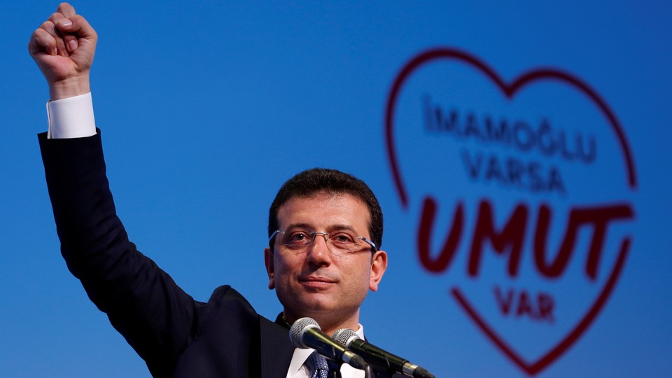 Ekrem İmamoğlu speaks at a rally with a heart graphic in the background.