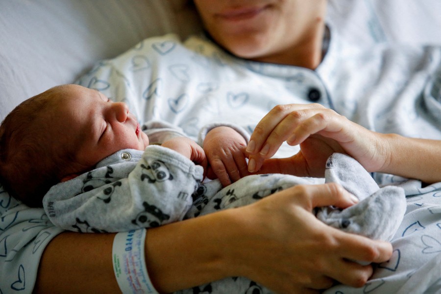 A newborn baby rests in his mother's arms in a bed.