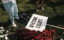 A photo of the legs of a person standing on a patch of grass next to a placard on the ground that reads "Vaccine Choice"