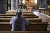 Older woman praying in an almost empty church