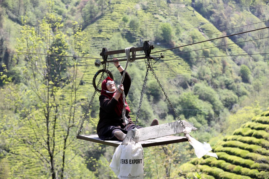 A woman sits on the platform of a basic hand-operated cable car suspended above a valley.