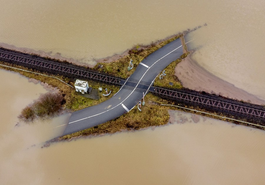Muddy water covers most of a road near a railroad crossing.