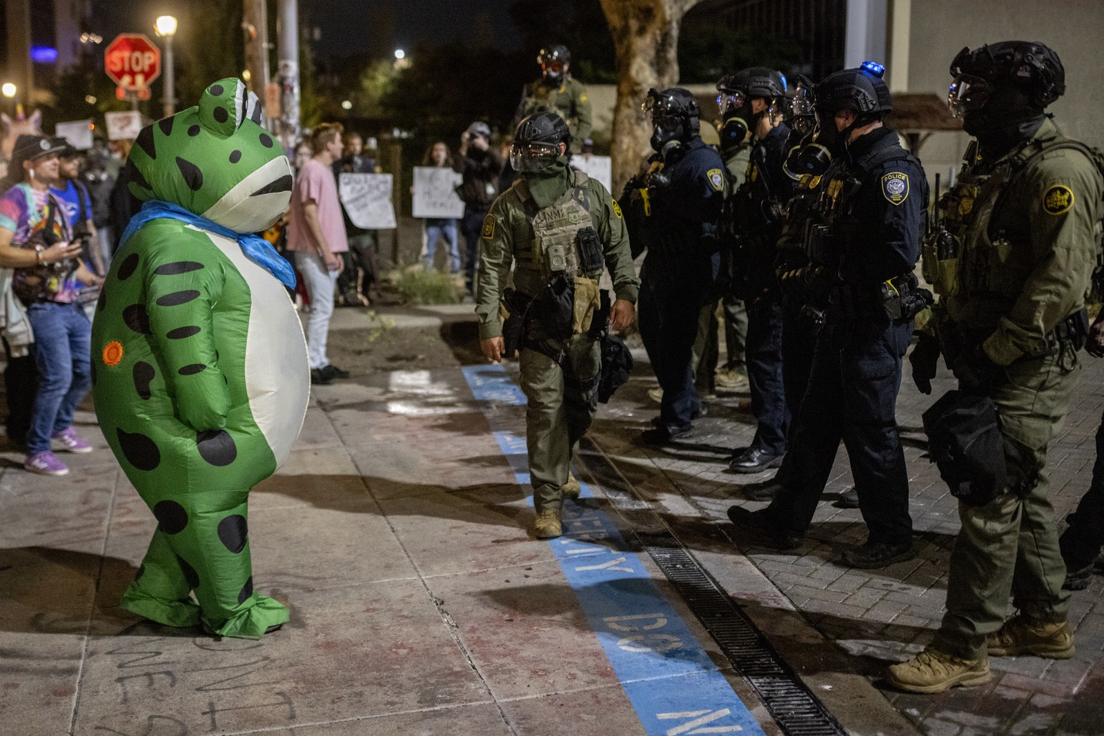 A protester in an inflatable frog costume faces off against several federal law enforcement officers.